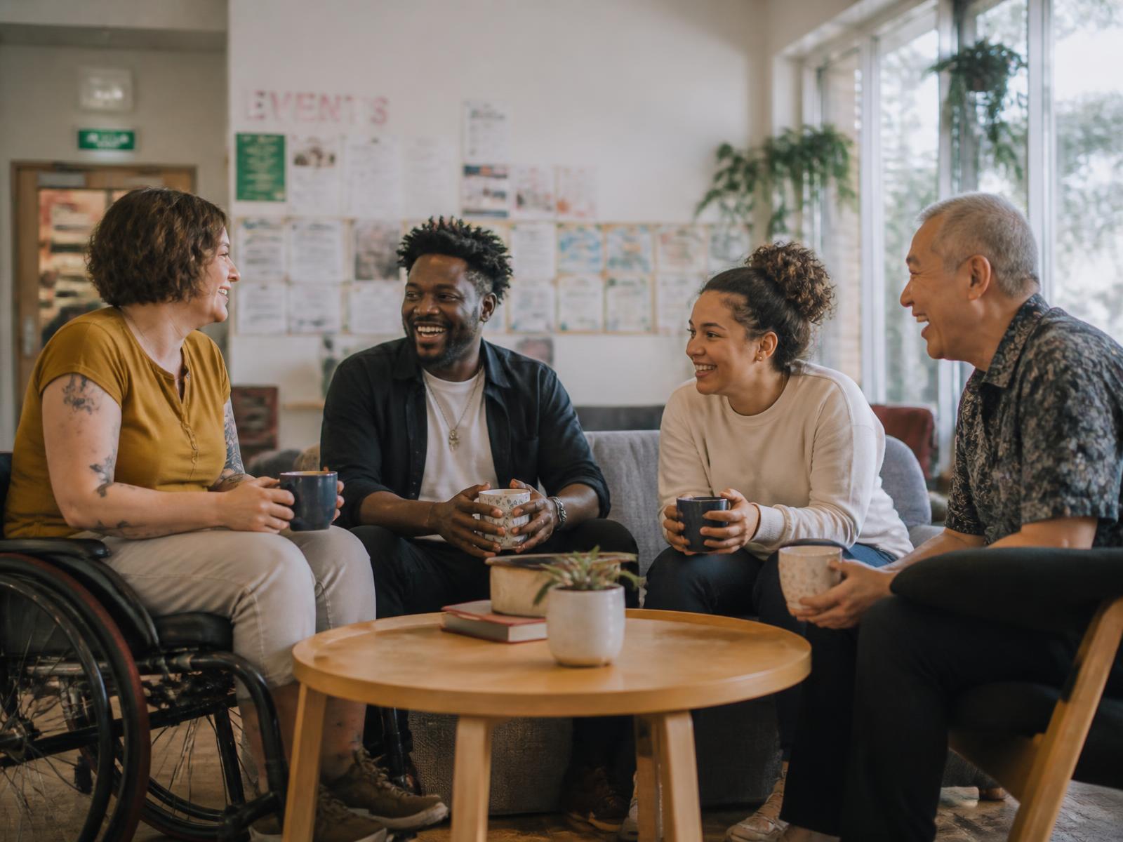 A group of adults from different backgrounds talking and laughing over coffee in a community center lounge